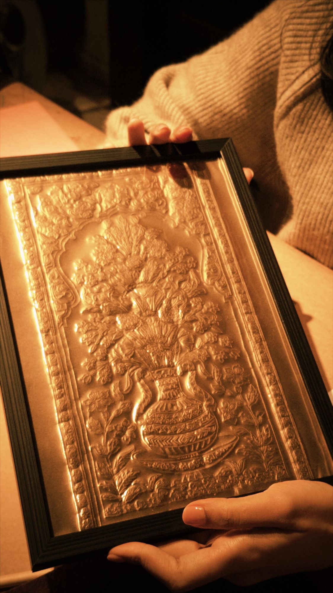 Hands holding a framed foil embossing of a flowering vase motif