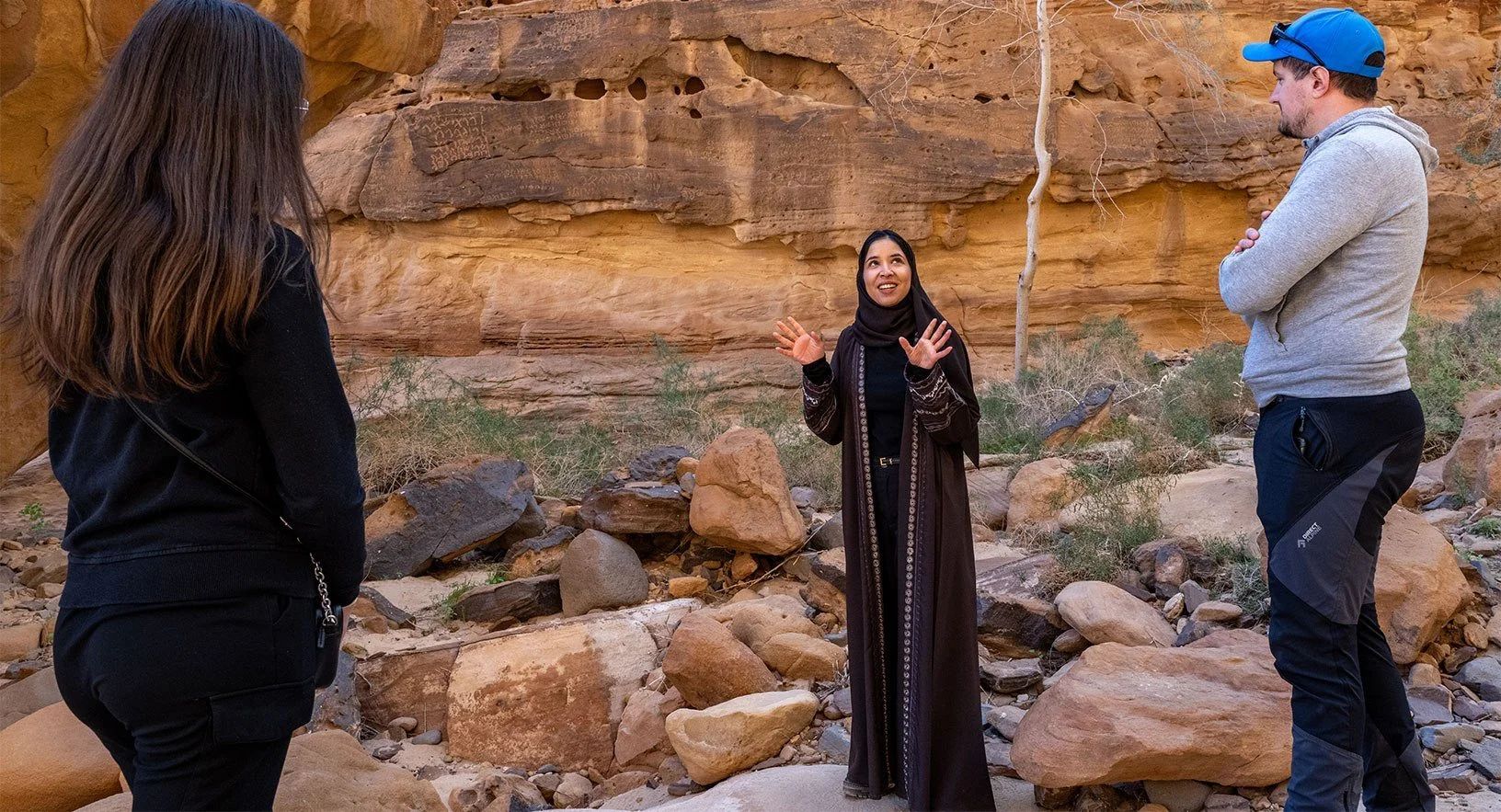 A rawi, a local storyteller, speaking with two visitors among the rocks and cliffs of AlUla, Saudi Arabia
