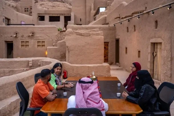 A group talking around a table in a courtyard of restored mud-brick buildings in AlUla